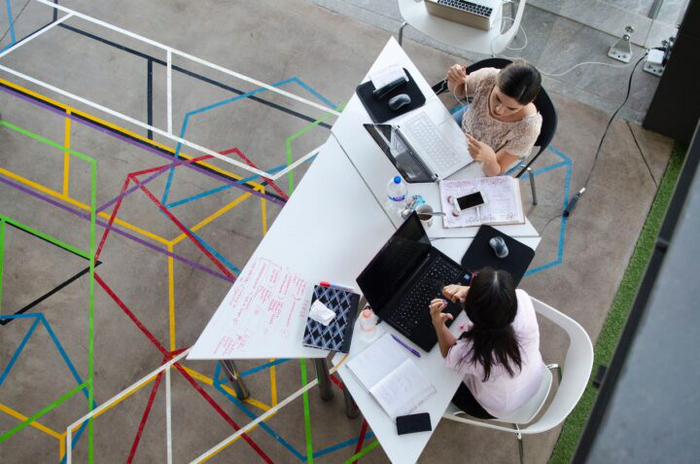 Two people working on laptops on a white table with an abstract background