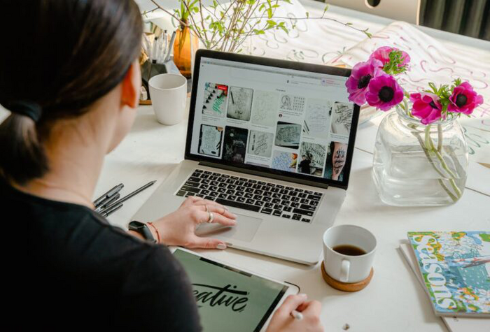 A person on a macbook searching a website. Flowers and a coffee sit next to the laptop