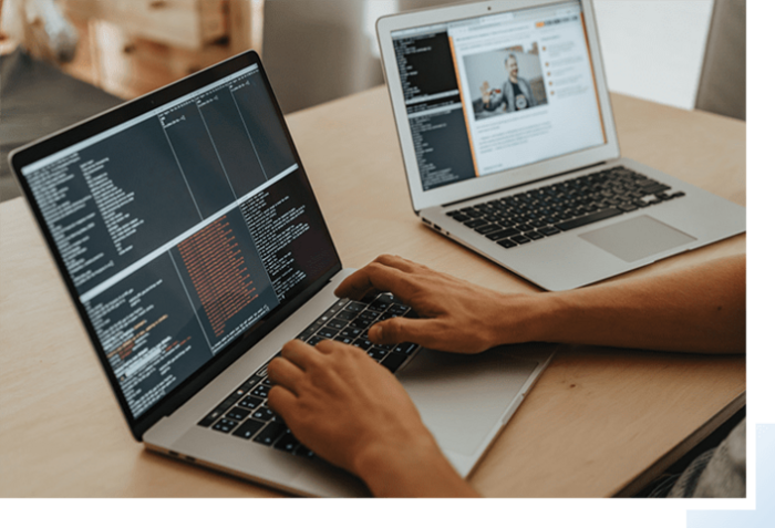 A person programming on a macbook laptop with another macbook sitting to their right