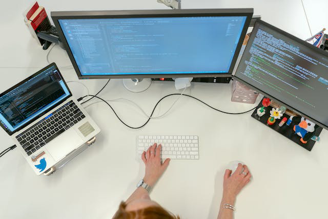 A person programming on a laptop with two screens on the side