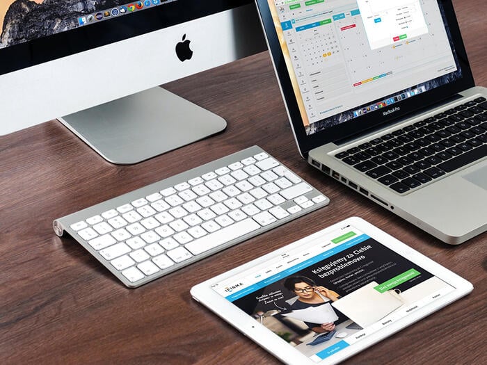 Mac, MacBook, and iPad placed on a wooden desk.